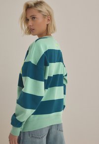 Zeleno-námornická pruhovaná mikina s volným střihem, žebrovanými manžetami a kulatým výstřihem. Na zadní straně je malý vyšívaný detail.