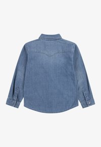 Jasnoniebieska, długosleeve'owa koszula dżinsowa z ostrym kołnierzykiem, guzikami przy mankietach i detalem w kształcie yoke na plecach. Gładka tekstura, swobodny design.