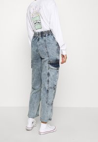Pantaloni cargo in denim azzurro chiaro con vita elastica, tasche laterali e leggera scoloritura; abbinati a una maglietta bianca a maniche lunghe con una grafica di popcorn.