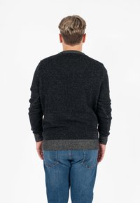Maglione grigio scuro con superficie testurizzata e orlo a coste, caratterizzato da un classico collo a giro e maniche lunghe, indossato con jeans blu.