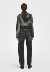Sweter w paski z dzianiny w kolorze czarnym i szarym, z wysokim kołnierzem i oversize'owymi rękawami. Połączony z ciemnoszarymi dżinsami z wysokim stanem.