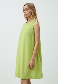 Abito verde senza maniche con una vestibilità ampia, realizzato in tessuto leggero. Presenta un collo rotondo e una tasca laterale. Texture liscia.