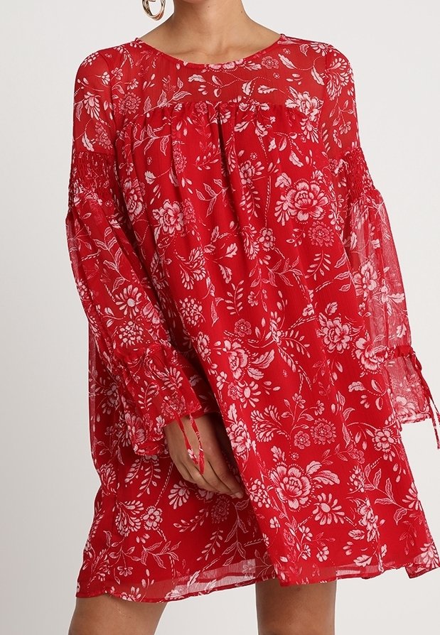 Robe florale rouge avec des manches longues en voile, présentant une coupe ample et un froncé au niveau du col. Motifs floraux dans des tons blancs et roses.