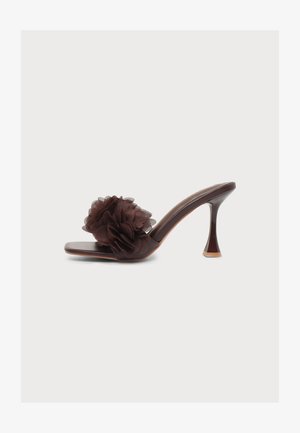 Sandalia mule de tacón alto de color marrón oscuro con tacón acampanado y gran decoración de flor de tela en la tira sobre los dedos.
