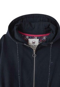 Hoodie zippé bleu marine avec une doublure intérieure florale, capuche ajustable, fermeture éclair argentée et logo brodé sur la poitrine. Texture douce et lisse.