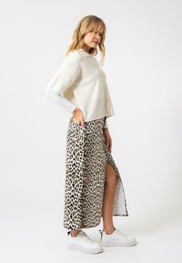 Slonový pletený top s krátkymi rukávmi a detailom gombíka; skombinovaný so sukňou s leopardím potlačou a bočným rázporkom; biele mohutné tenisky.