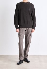 Textured dark brown ribbed sweater, loose fit, paired with light gray cargo pants featuring pockets. Black polished shoes complete the outfit.
