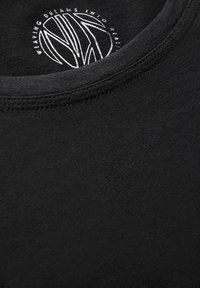 T-shirt nera in cotone con scollatura rotonda, caratterizzata da una stampa grafica bianca all'interno del colletto che recita "TRAMANDO SOGNI NELLA REALTÀ."