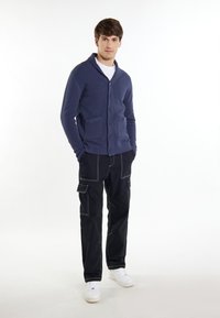 Marinblå ribbad cardigan med sjalkrage och knappar, i kombination med svarta cargo-byxor med fickor och vita sneakers.