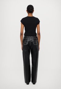 Black leather pants with a loose fit and white stitching, paired with a fitted black short-sleeve top. Seen from the back.