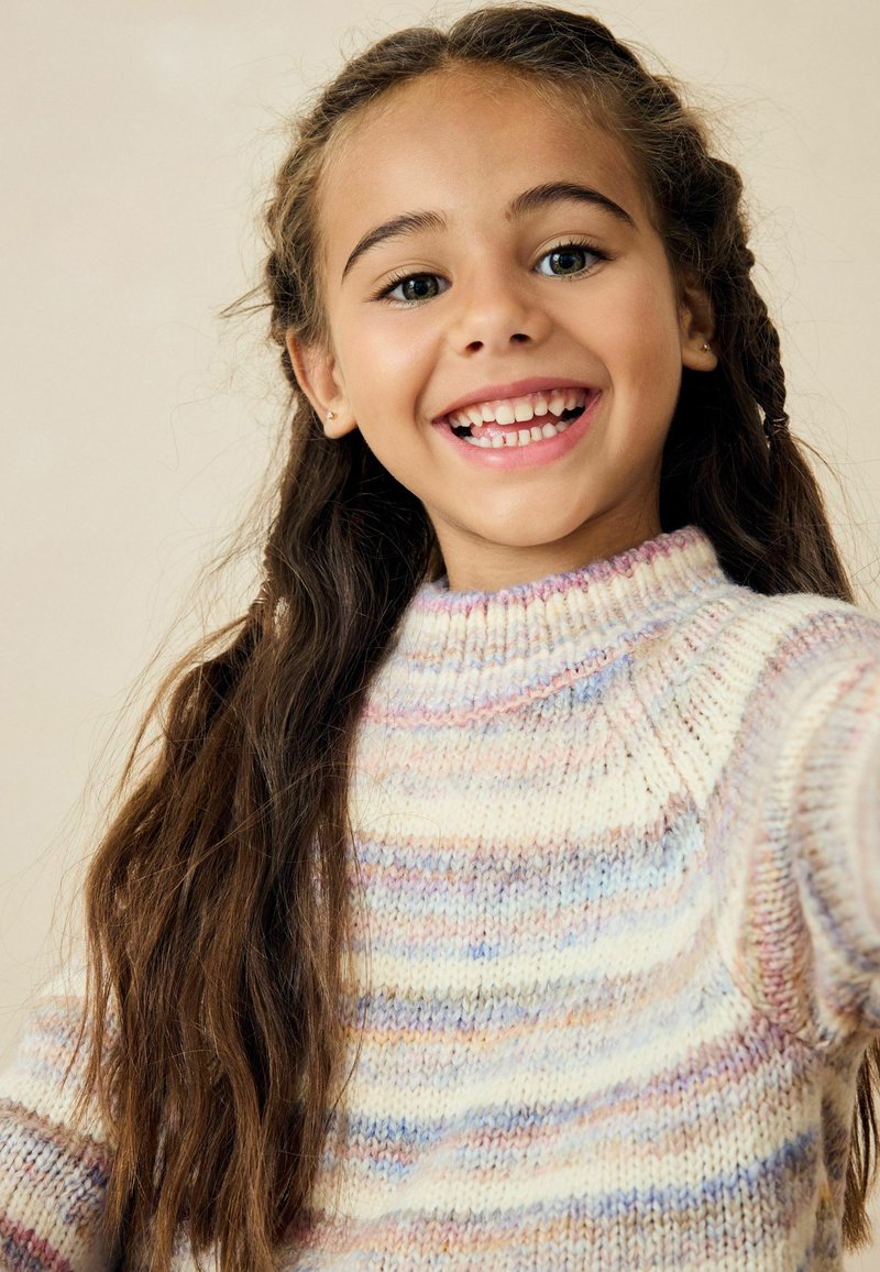 Monivärinen, neulepaita korkealla kauluksella, jossa on vaaleita raitoja sinisen, vaaleanpunaisen ja kermanvärisen sävyissä. Pitkät, suorat hiukset.