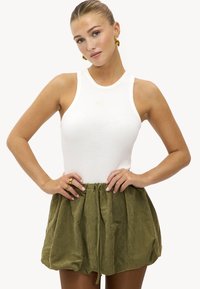 Débardeur blanc côtelé associé à une jupe ample vert olive avec taille à cordon. La jupe est en tissu doux et texturé.