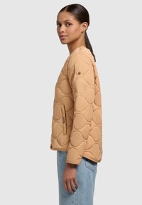 Giacca trapuntata beige con un motivo ondulato tondo, dotata di una tasca laterale e un piccolo logo sulla manica, realizzata in un tessuto morbido e testurizzato.