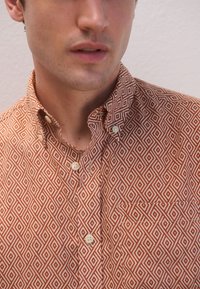 Camicia con bottoni a pressione con motivo a rombi rossi e bianchi, materiale in cotone, colletto standard, due bottoni all'altezza del collo, dettaglio discreto della tasca.