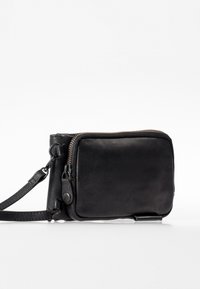 Borsa a tracolla nera in pelle con una texture liscia, scomparto con zip, tracolla rimovibile e sottili accenti metallici. Design compatto.