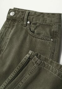 Gros plan sur un jean en denim vert olive montrant la poche avant, la boucle de ceinture, le bouton et les coutures détaillées.