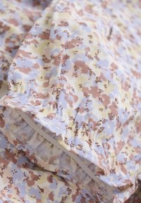 Stoff mit floralem Muster in Pastellfarben (Gelb, Blau, Rosa) und weicher Textur. Der geraffte Rand verleiht dem Design eine besondere Note.