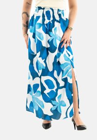 Falda maxi con un patrón floral en azul y blanco, hecha de tejido ligero, que presenta una abertura alta y una cintura elástica. Llevada con tacones negros.