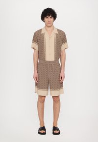 Set de chemise à manches courtes et de shorts en marron et beige, avec un motif géométrique, un col plat et une ceinture élastique.