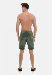 Shorts en denim verts avec des ourlets retroussés, dotés de poches arrière et d'un logo en patch. Le tissu a une texture douce et une finition délavée.