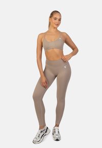 Beige treenivaatteet sisältävät istuvan urheil bra:n, jossa on ohuet hihnat, sekä korkeavyötäröiset legginsit. Materiaali on sileä ja siinä on hieno venyvyys, ja se sisältää logon.