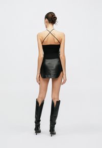 Μαύρο πλεκτό τοπ με λουριά που διασχίζουν την πλάτη, σε συνδυασμό με μαύρη δερμάτινη μίνι φούστα. Μαύρες μπότες μέχρι το γόνατο με μυτερές άκρες ολοκληρώνουν την εμφάνιση.