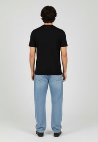 Czarna koszulka z krótkim rękawem i okrągłym dekoltem, z subtelnym logo na plecach. Do tego jasnoniebieskie, luźne dżinsy.