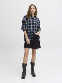 Marine rutete oversized skjorte med knapper, svart kordfløyelskjørt og knelange svarte skinnstøvler med blokkhæler. Jevn overflate generelt.