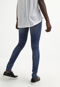 Úzké džíny z denimu v středně modrém praní s hladkou texturou, s mírným pasem a minimálními doplňky, spárované s černými teniskami.