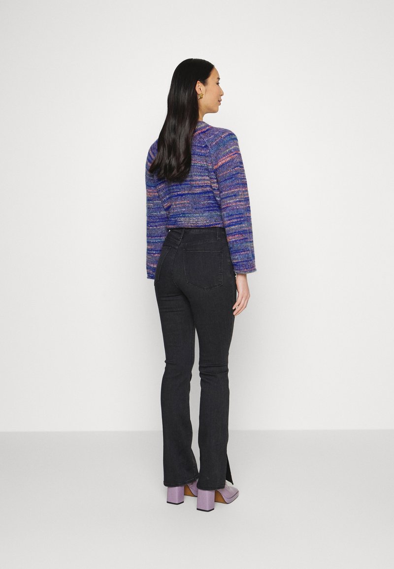 Sweater de malha cropped, multicolorido em tons de roxo, combinado com jeans pretos ajustados. A modelo usa sapatos lilás de salto bloco, mostrando uma divisão mínima na bainha.