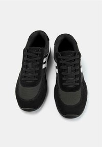 O pereche de adidași negri cu dungi laterale albe și șireturi negre, văzuți dintr-o perspectivă de sus pe un fundal alb.