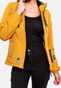 Veste jaune à capuche en matière douce avec fermetures éclair et poches. Comprend une doublure noire et des accents de logo, associée à un pantalon noir.