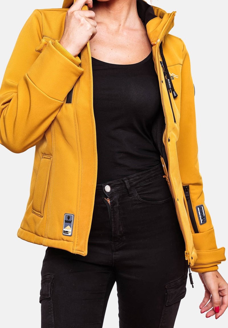 Veste jaune à capuche en matière douce avec fermetures éclair et poches. Comprend une doublure noire et des accents de logo, associée à un pantalon noir.