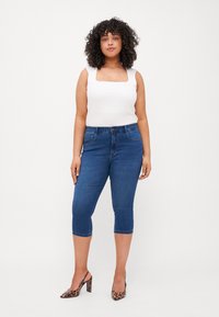 Blå denim capri jeans, mid-rise med lommer foran, kombinert med en hvit ermeløs topp med firkantet utringning.