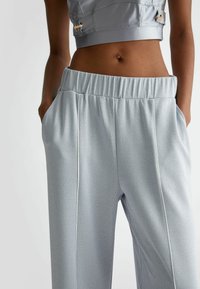 Pantaloni atletici grigio chiaro in tessuto texture, con vita elastica, tasche laterali e piping bianco lungo le cuciture.