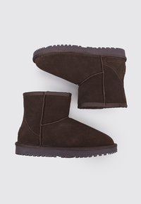 Botines de ante marrón con punta redonda, detalles de costura y suela de goma texturizada, que presentan un diseño sencillo y funcional.