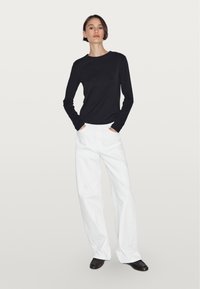 Black long-sleeve top with a round neckline, paired with loose-fitting white pants and black footwear. Simple, clean design with no patterns.