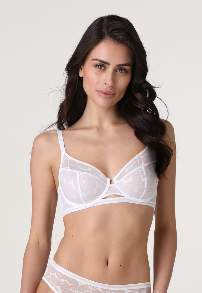 Reggiseno bianco con sovrapposizione di pizzo floreale, supporto con ferretto, spalline regolabili e una fascia liscia con un dettaglio a chiave al centro.
