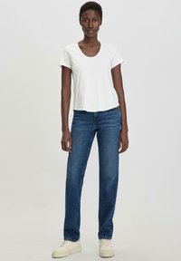 T-shirt bianco a maniche corte con scollo a barca, abbinato a jeans blu a gamba dritta. Indossato con sneakers color crema.