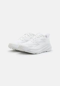 Vita sportskor med en andningsbar mesh-överkonstruktion, texturerad design, vadderade sulor och platt snörning. Rundad tå och robust konstruktion.