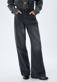 Breda ben, mörkgrå denimbyxor med hög midja, sidofickor och knappstängning. Tyget har en lätt urtvättad textur.