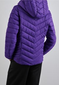 Fioletowa puchowa kurtka z kapturem, z chevronowym wzorem pikowania, gładką teksturą i elastycznymi mankietami, noszona na ciemnych spodniach.