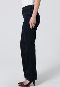 Donkerblauwe spijkerbroek met een rechte pijp, subtiele stitchingdetails en zijzakken. Gecombineerd met kastanjebruine hoge hakken.