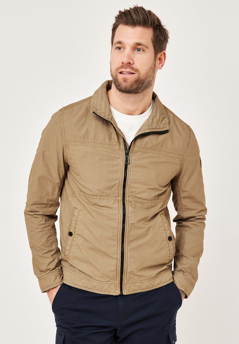 Light brown jacket with a stand-up collar, features two front pockets and a zippered closure. Smooth texture with subtle stitching details.