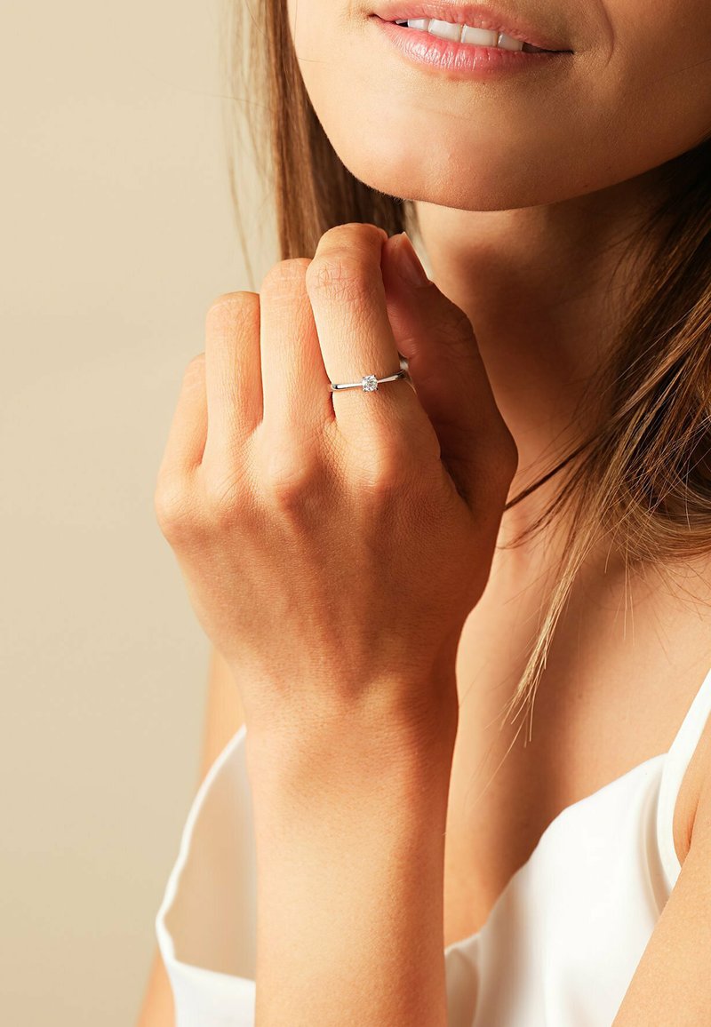 Sterling silver ring with a round clear stone, slim band, worn on a hand with light skin. Natural nail texture visible.