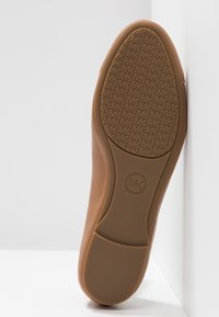 Semelle d'une chaussure beige présentant un motif texturé du logo MK sur l'avant-pied et un talon lisse avec un emblème circulaire MK dans la zone de la voûte plantaire.