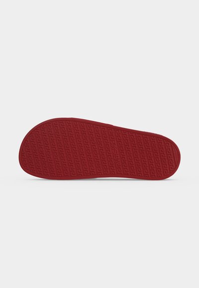 Semelle d'une chaussure rouge avec un motif géométrique texturé et le nom de la marque "VERSACE" embossé au centre.