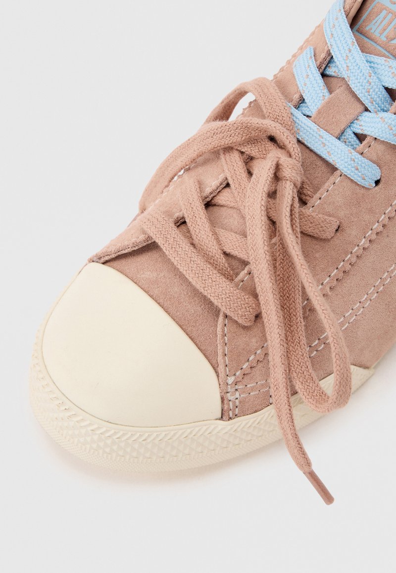 Rosa Wildleder-Sneaker mit cremefarbenem Gummizehenschutz, gemusterten Schnürsenkeln in Pink und Blau sowie sichtbaren Nähten vor hellem Hintergrund.