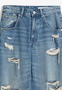 Blue denim jeans with multiple distressed rips and frayed edges on front thighs, featuring front pockets and a button closure waistband.
