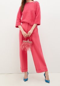 Pehmeä vaaleanpunainen neule, jossa on 3/4-hihat; vaaleanpunaiset leveälahkeiset housut, joissa on korkea vyötärö; pieni vaaleanpunainen käsilaukku, jossa sulka-akselentteja; siniset korot.